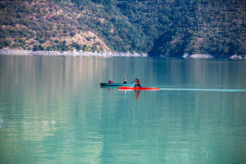 Two men are waiting in one boat while another man rows in a separate kayaking boat. This scene captures the camaraderie and patience often found in water sports.