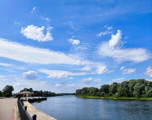 Serene landscape with fluffy clouds over a calm river surrounded by lush greenery. Beautiful summer landscape river surrounded by green vegetation