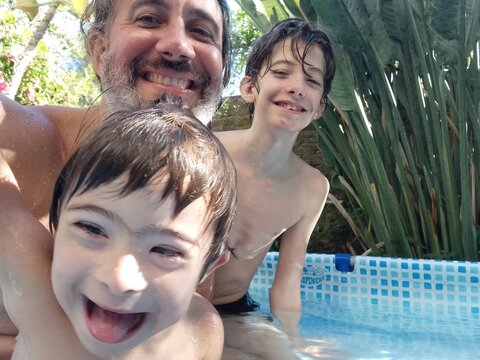 Padre e hijos  uno con s&iacute;ndrome Down, se divierten al al aire libre en pileta de lona jugando