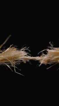 Vertical video. Close-up of a frayed rope on the verge of snapping, showing tension and stress in the fibers against a black background.
