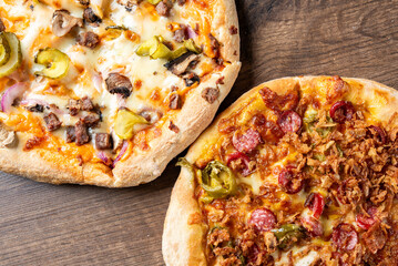 Two delicious pizzas on a wooden table. One features pepperoni, green peppers, and crispy onions, while the other is topped with mushrooms, jalapeños, and savory meats. Perfect for sharing!