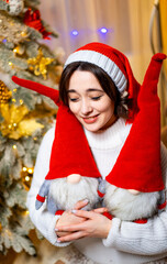 Celebrating Christmas with joyful gnomes. A woman wearing a festive hat embraces two cheerful gnome plush toys during the holidays.