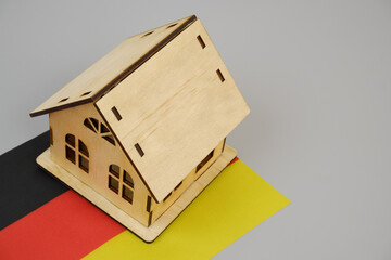 Real estate in Germany. Wooden house model and German flag on gray background.	