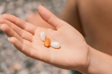 A person is holding a handful of nuts in their hand. The nuts are of different sizes and shapes, and they appear to be almonds. The person seems to be enjoying the nuts and is likely to eat them soon.