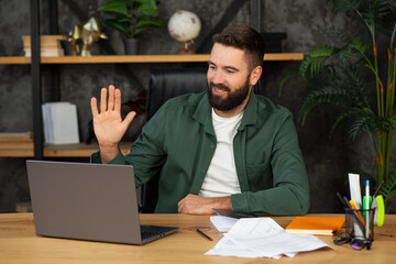 Young happy man freelancer or entrepreneur have video conference, shows a greeting gesture, working...