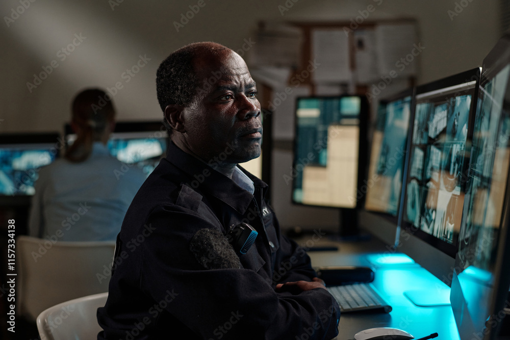 Poster serious african american security guard concentrating on cctv video on screen of computer while sitt