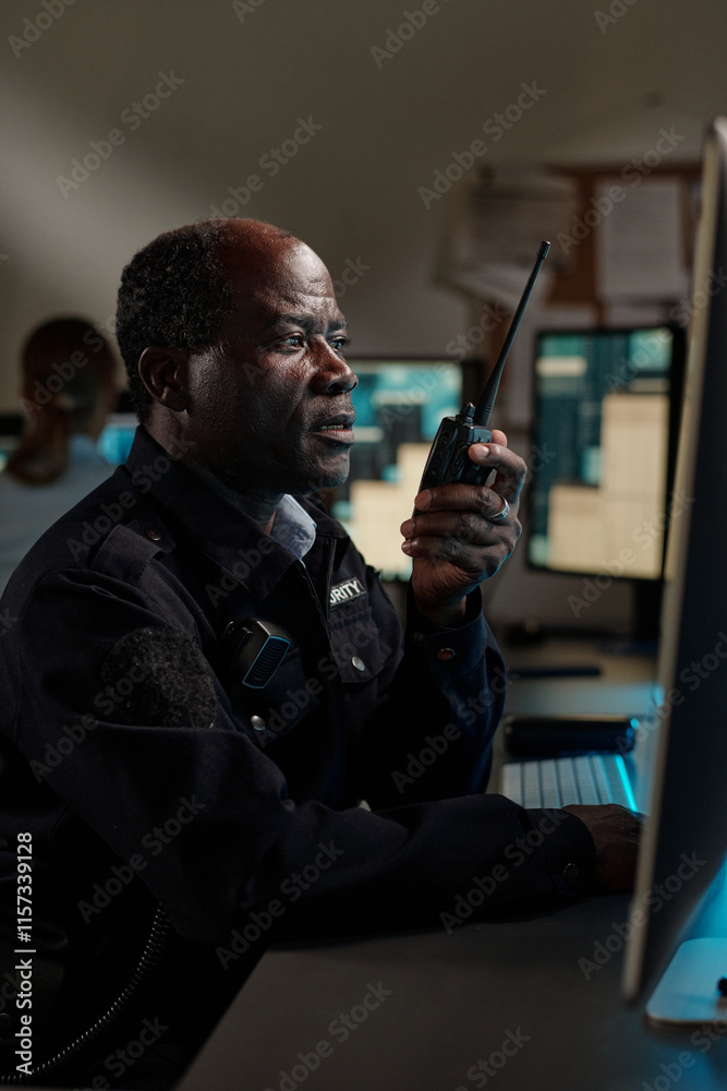 Poster mature african american security guard in black uniform looking at desktop computer screen while spe