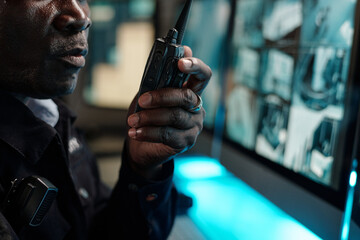 Hand of mature male guard speaking in walkie-talkie in front of computer screen while reporting...