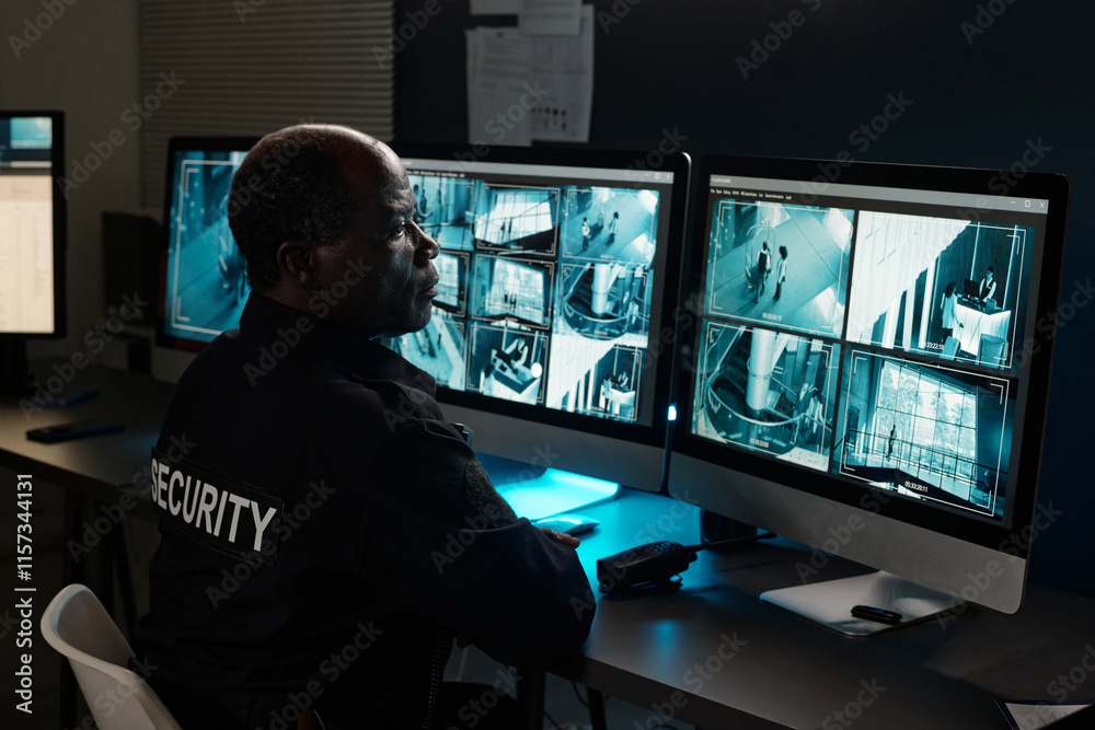 Poster mature male security guard looking at one of several desktop computer screens with cctv video system