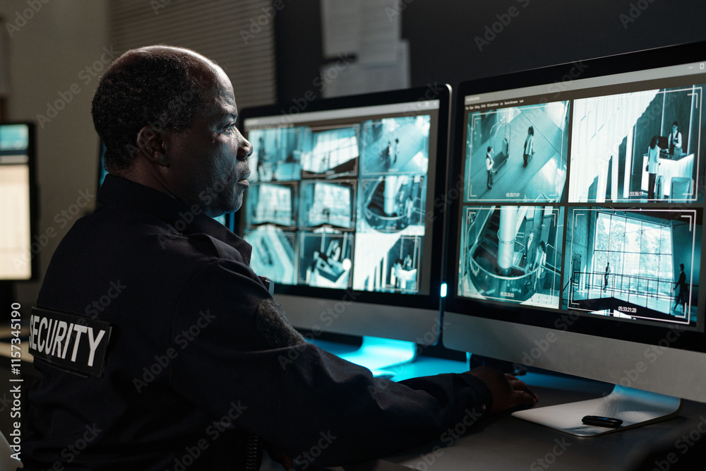 Poster serious security guard concentrating on watching cctv video while looking at one of several desktop 