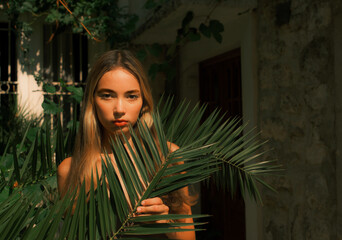 A woman is standing in front of a building with a leafy green plant in her hand