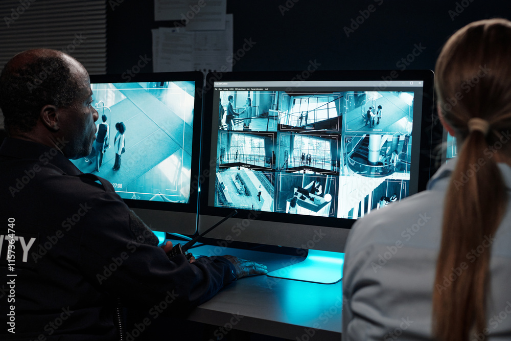 Poster young and mature intercultural security guards in uniform sitting in front of desktop computers with