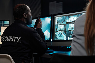 Mature African American man talking in radio transceiver and looking at computer screen with cctv...