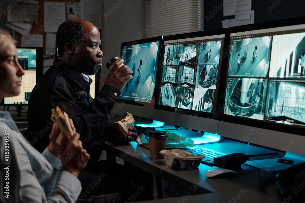 Poster focus on mature male security guard with cup of coffee and sandwich sitting by workplace in front of