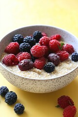 bowl of creamy millet porridge with fresh berries resting on matte yellow background under bright studio lighting