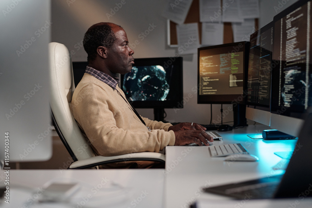 Aufkleber Side view of serious mature male programmer typing on computer keypad while decoding data on screen while sitting by desk