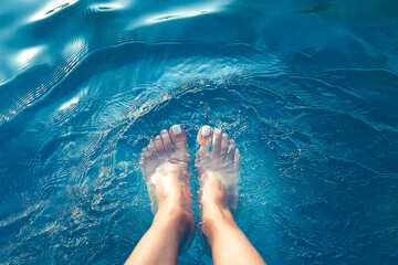 female feet in the water, beautiful bright blue water, texture of the blue water surface
