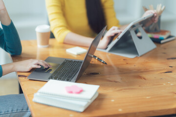Collaborative Workspace: Two young women engage in focused work using laptops and tablets at a modern wooden desk.  The scene exudes calm productivity and teamwork. 
