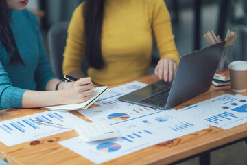 Collaborative Analysis: Two female business professionals work together on a project, analyzing data on a laptop and taking notes. The image showcases teamwork, focus, and strategic thinking.  