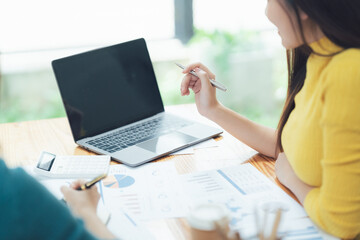Business Collaboration: A woman in a yellow top points at a laptop screen, discussing a financial...