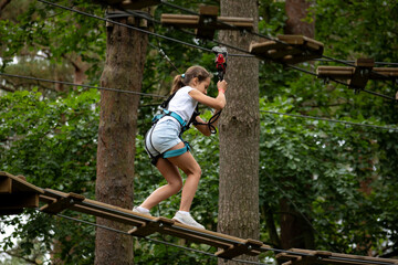A girl skillfully traverses a high rope course, focused on her balance amid tall trees. Nature...