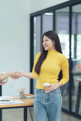 Businesswoman Handshake: A confident young Asian businesswoman in a yellow sweater and jeans shakes...
