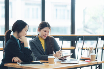 Businesswomen Collaboration: Strategic Discussion. Two focused Asian businesswomen collaborate on a project, reviewing documents at a modern office table.