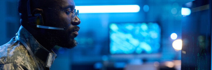 Header of serious male military operator in headset, eyeglasses and camouflage uniform looking at computer screen © pressmaster