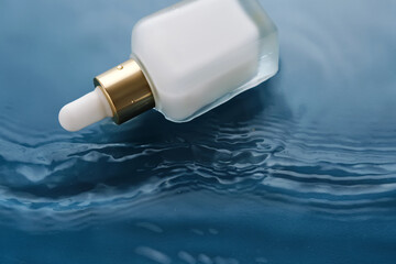 Bottle with white moisturizing serum in water on blue background.