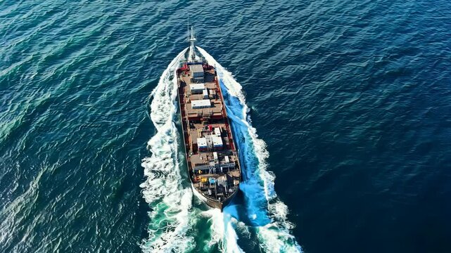 Cargo ship sailing through clear blue waters, viewed from above with visible waves trailing behind, Logistics, maritime shipping, sea freight transportation, international trade, 