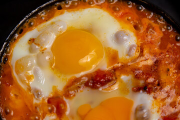Shakshuka with tomatoes, peppers and onions is fried in a frying pan. Close-up