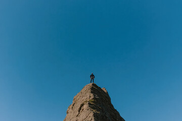 A man stands on a mountain top, looking out over the vast blue sky