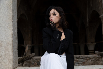 Young woman with black hair, dressed in black Gothic style, in a ruined church.