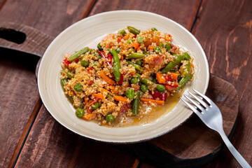 Couscous with vegetables in sauce on a plate on the table next to a fork