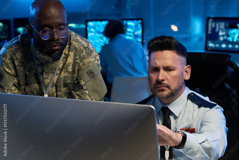 Poster Serious mature male operator in uniform looking and pointing at desktop computer screen during presentation of online information
