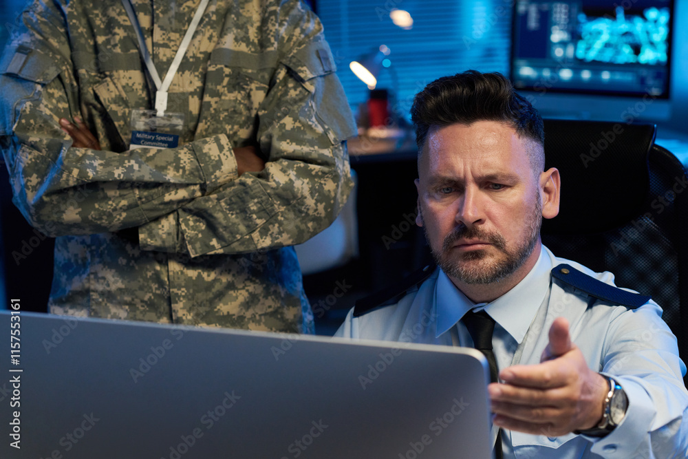 Leinwandbilder Serious mature man in uniform looking at desktop computer screen with misunderstanding while sitting next to colleague