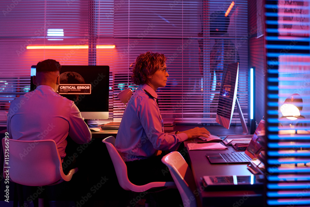 Poster side view of serious mature female officer in uniform sitting by desk in front of computer monitor a