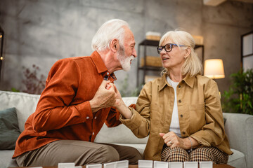 Senior happy couple husband and wife play dominoes together at home