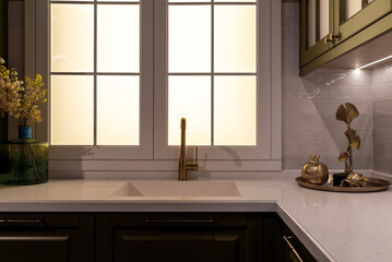 Brass kitchen faucet on a white quartz countertop near a window
