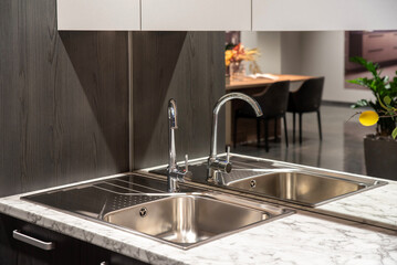 Modern chrome faucet with mirrored backsplash and steel sink in a kitchen
