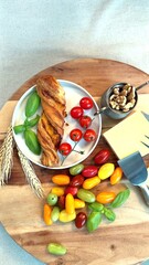 Rustic wooden board with eco-friendly ingredients: cherry tomatoes, cheese wedge, golden flaky pastry, basil. Promotes clean, healthy countryside breakfast, sustainable, natural lifestyle concept.