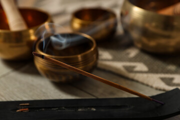 Incense stick smoldering in holder and tibetan singing bowls on floor, closeup