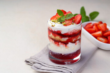 Tasty trifle dessert. Strawberries, sponge cake and whipped cream in glass on beige table, space for text