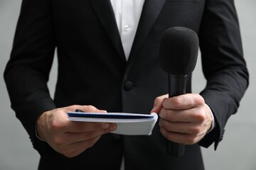 Journalist with microphone and notebook on grey background, closeup