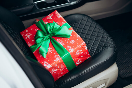 Festive gift box with green ribbon on car seat interior