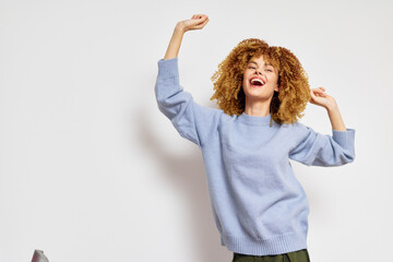 Happy woman celebrating joyfully in a soft blue sweater against a minimalist white background,...