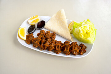 Cig kofte (raw meatball) with lettuce, tomato, pickle and lemon, hot Chee kofta. Turkish local raw food concept.Table scene of assorted take out or delivery foods. Doritoslu duble cig kofte durum.