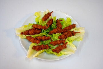 Cig kofte (raw meatball) with lettuce, tomato, pickle and lemon, hot Chee kofta. Turkish local raw food concept.Table scene of assorted take out or delivery foods. Doritoslu duble cig kofte durum.