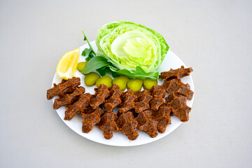 Cig kofte (raw meatball) with lettuce, tomato, pickle and lemon, hot Chee kofta. Turkish local raw food concept.Table scene of assorted take out or delivery foods. Doritoslu duble cig kofte durum.