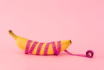 Banana wrapped with pink measuring tape on pink background ,weight loss or sex education concept